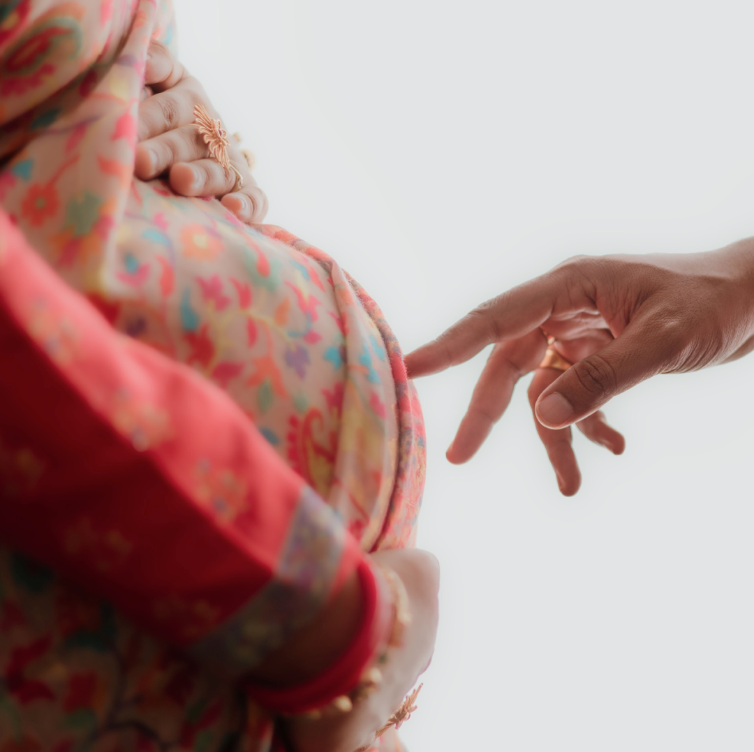 A hand reaching towards an expectant mother in a pink saree